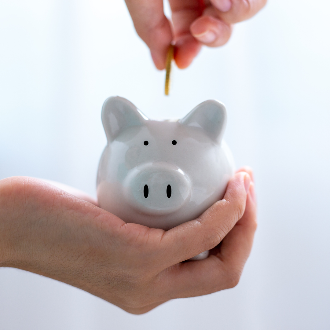 Hand wirft Münze in weiße Schweine-Spardose